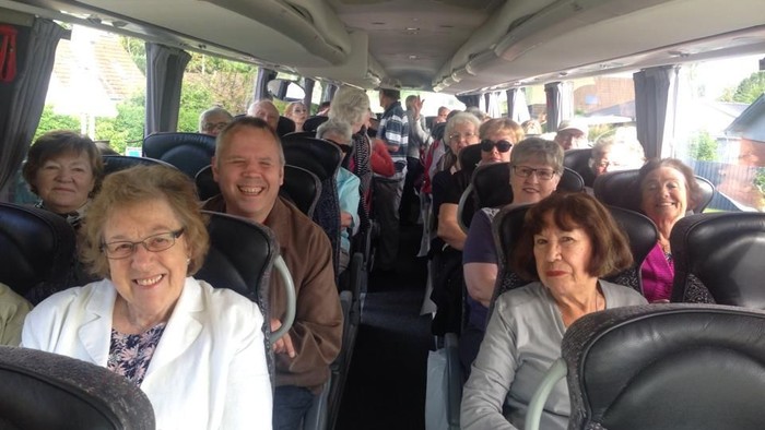 En gruppe af ældre personer sidder i en bus og smiler til kameraet.