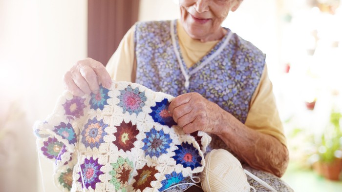 En gammel kvinde sitter ved vinduet og laver blomsterstøvletæppe.