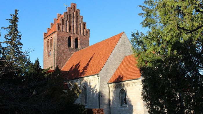 En kirke med høj tårn og røde tag, omgivet af træer