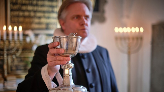 Mand i mørkt tøj holder en sølv kalk i kirke