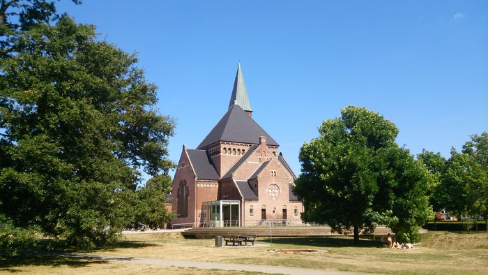 En rød kirke med spir med træer og klar himmel i baggrunden