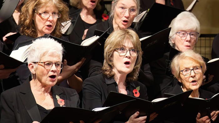 A group of elderly women singing in a choir, holding sheet music.