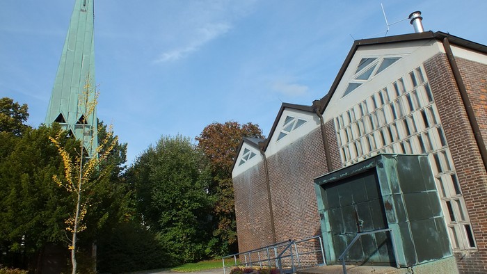 Das Bild zeigt eine Kirche mit hohem Turm und modernem Anbau.