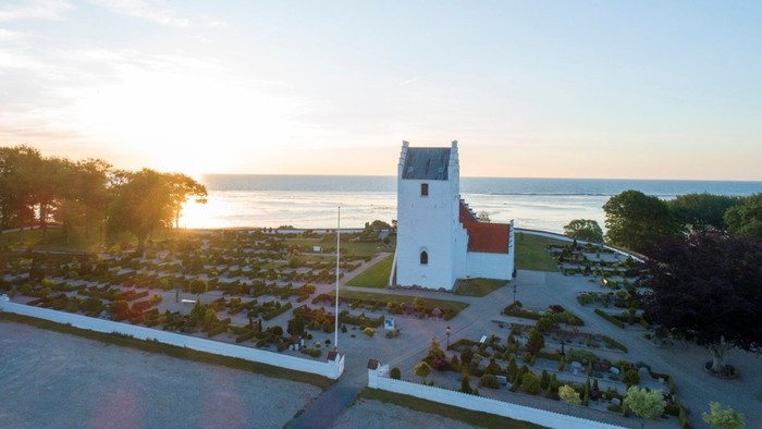 En hvid firkantet fyrtårn ved stranden med solnedgang i baggrunden