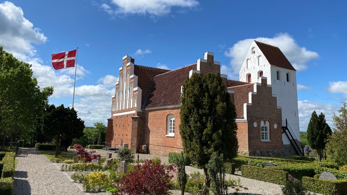 En rød og hvid murstensbygning med flagstang og have