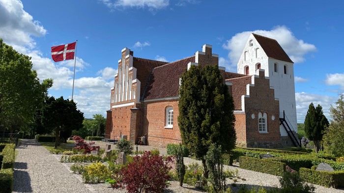 En rød og hvid murstensbygning med flagstang og have