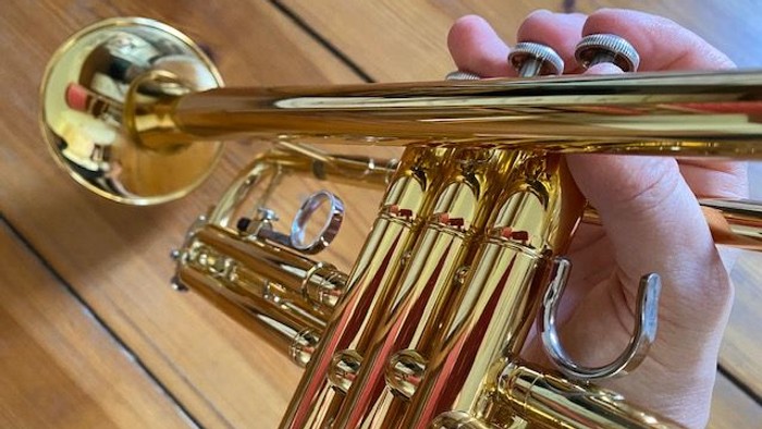 Eine Hand hält eine goldfarbene Posaune auf einem Holzboden