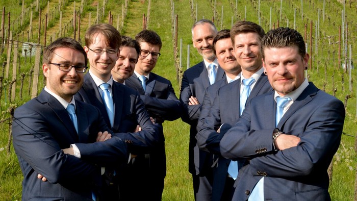 Ein Gruppe von Männern in Anzügen posiert vor einem Weinberg