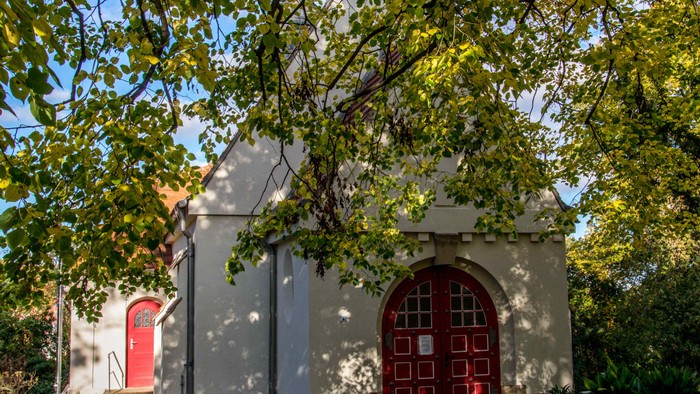 Kleine Kirche mit zwei roten Türen und umgeben von Bäumen und Büschen