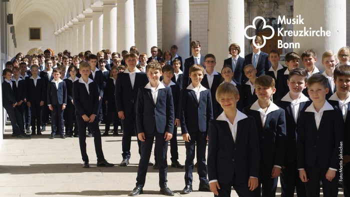 Eine Gruppe von Jungen in Anzügen steht vor einem Gebäude mit Säulen.