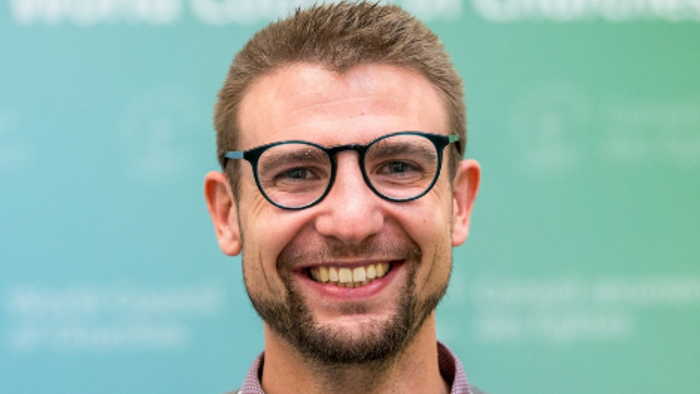 Mann mit Brille und Lanyard vor grünem Hintergrund