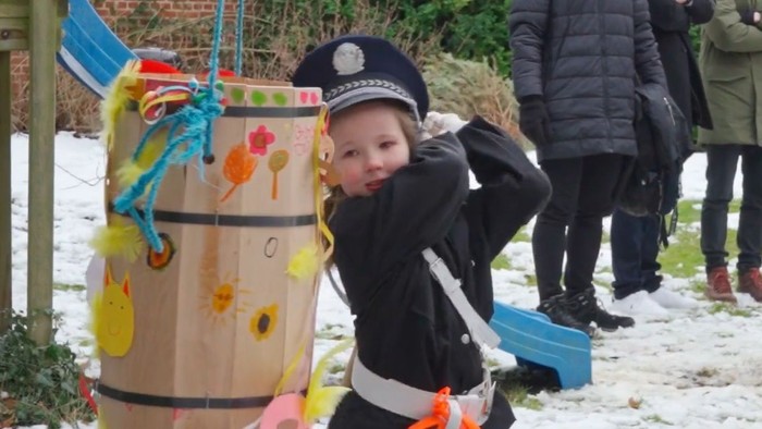 Et barn i politiuniformskostume leger med en pyntet tønde til en udendørs begivenhed i sneen.