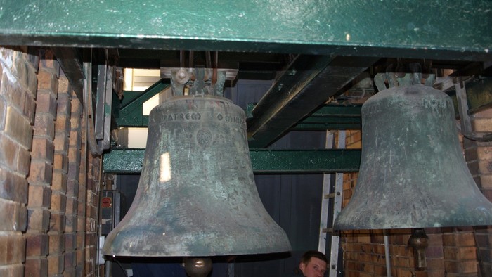 Zwei Glocken hängen an einem grünen Metallrahmen in einem Turm.