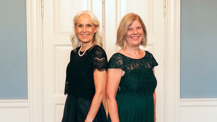 To kvinder står sammen, begge med smilende ansigter.