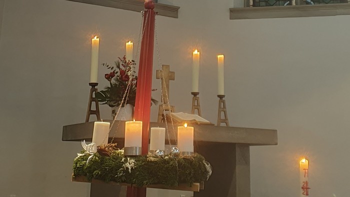 Ein Kircheninneres mit einem großen Kreuz, Kerzen und buntem Glasfenster