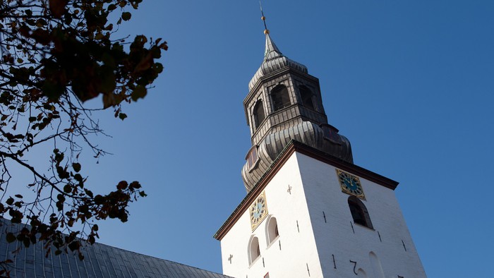 En hvid kirke med sort spire og guldtop under et klarblåt sky.