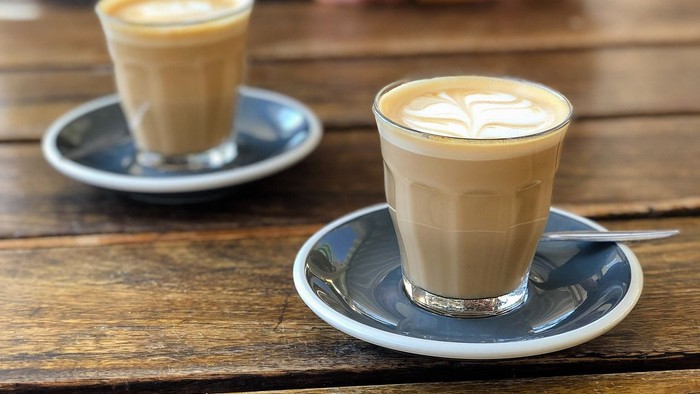 Zwei Tassen Kaffee auf Holztisch, Person nutzt Handy