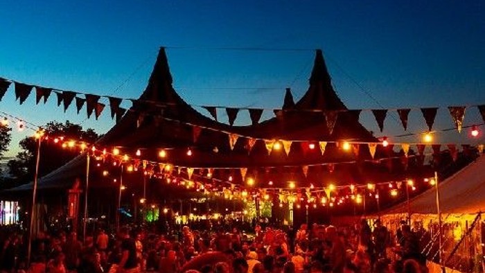 Large crowd gathered under string lights and tents at night.