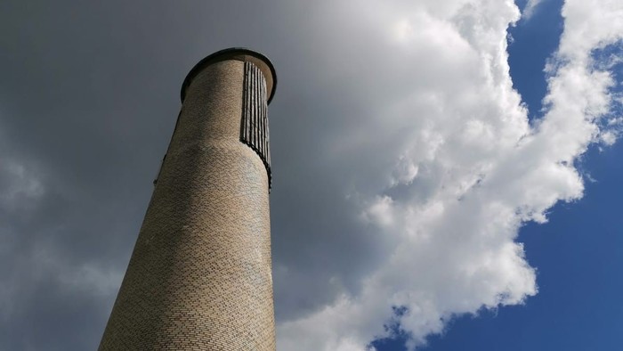 Hoher Schornstein vor blauem Himmel mit weißen Wolken.