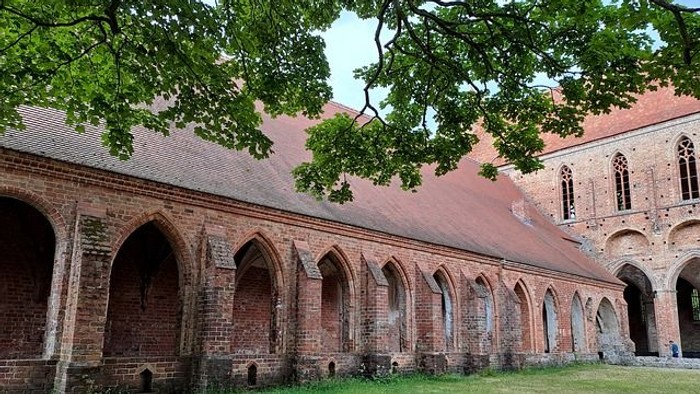 Altehrwürdige Ziegelgebäude mit Bogengängen und grünem Rasen davor
