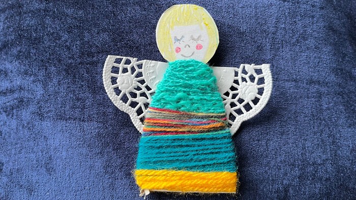 Mit bunter Wolle umwickelte Engelsfigur auf blauem Hintergrund