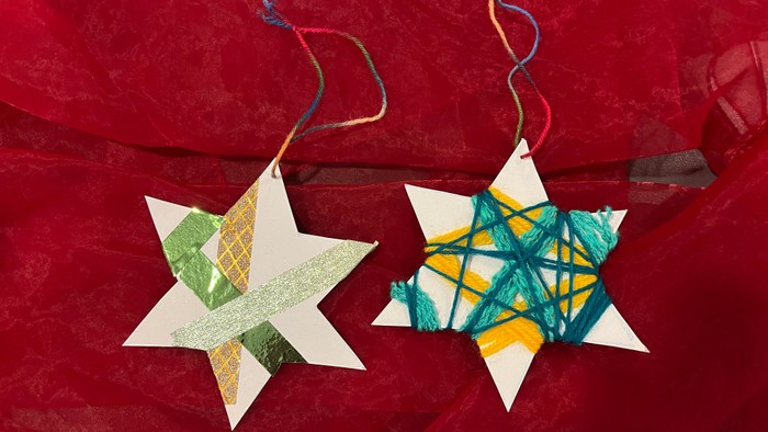 Zwei Sterne aus Pappe, mit bunter Wolle umwickelt und buntem Klebeband beklebt, zum Aufhängen auf rotem Hintergrund