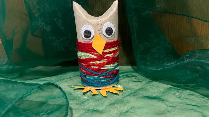 Mit bunter Wolle umwickelte Klorolle als Eule gestaltet auf grünem Hintergrund.