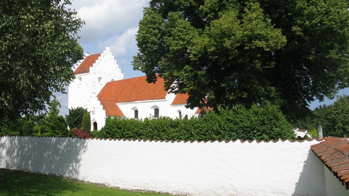 Et hvidt kirkebygningskompleks med røde tag og omgivet af grønne træer og en hvid mur