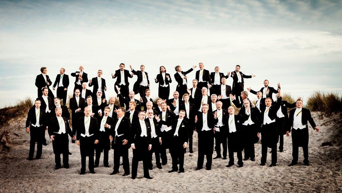 En stor gruppe mænd i formelle tøj samlet på en sandstrand