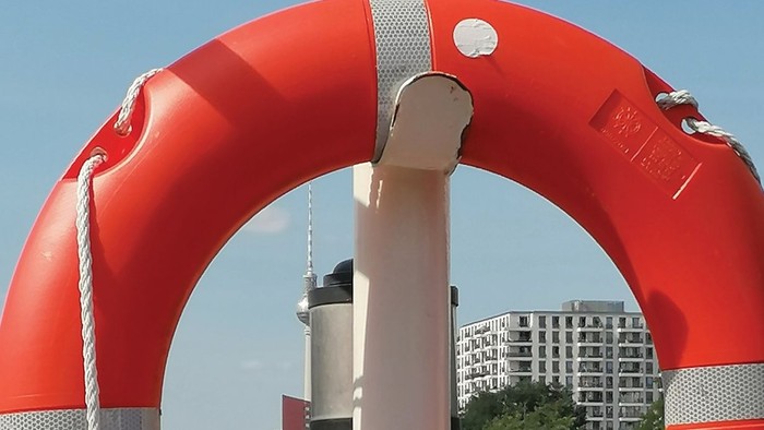 Ein großes rotes Rettungsboot an einem Pfahl, im Hintergrund ein Leuchtturm und Gebäude.