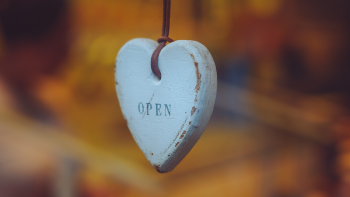 Ein weißes herzförmiges Schild mit der Aufschrift *„OPEN“*, das in einem Schaufenster hängt.