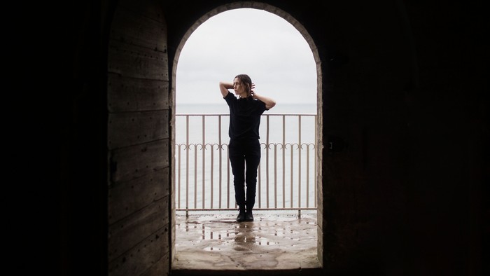 En person står ved et balustrade og kigger ud over havet gennem en buet åbning.