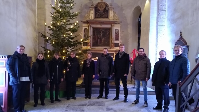 Eine Gruppe von Menschen steht vor einem geschmückten Weihnachtsbaum in einer Kirche.