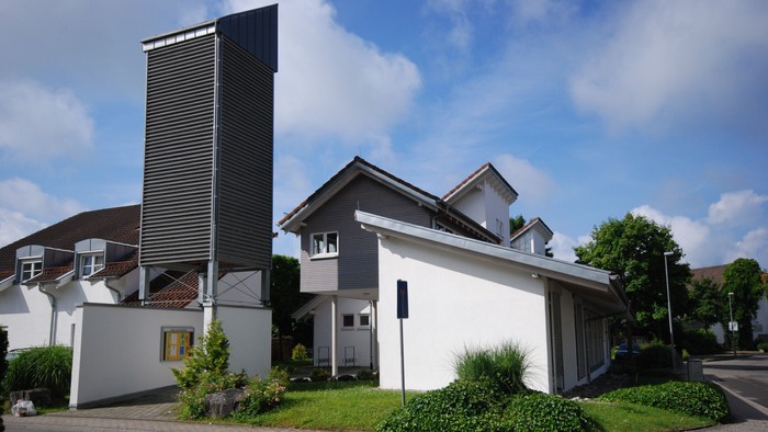 Ein modernes Gebäude mit hohem Kamin und weißer Fassade, umgeben von grünem Rasen und Bäumen.