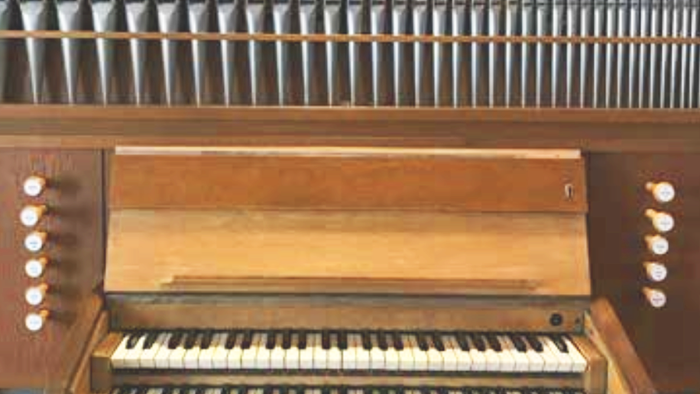 Ein hölzernes Harmonium mit zwei Klaviaturen und Metallpfeifen im Hintergrund