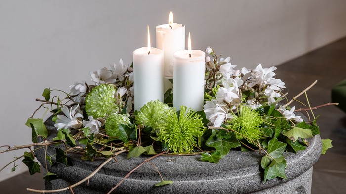 En pyntet stenskovlunge med tre lysende lysekønge omgivet af grønne og hvide blomster.