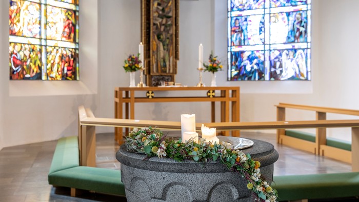 Kirkeinteriør med alter, bænke og font med blomster.