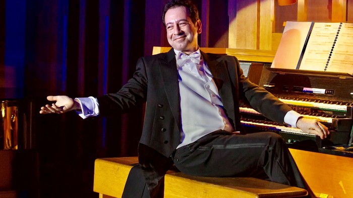 Mand i formel klædning sidder ved et piano og smiler.