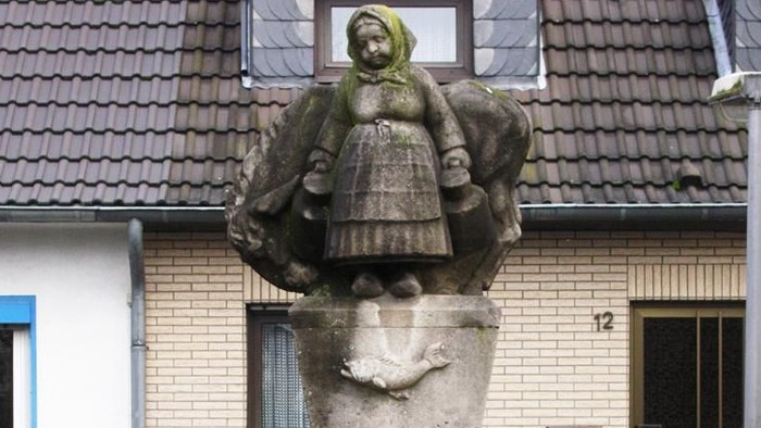 Steinstatue einer Frau auf einem Sockel vor einem Haus