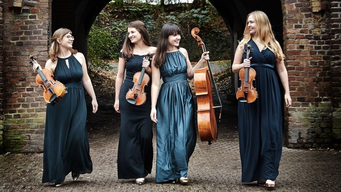 Vier Musikerinnen in historischen Kleidern spielen Geigen und Cello vor einem Torbogen.
