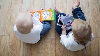 Zwei Kinder spielen auf dem Boden mit Büchern und einem Tablet.