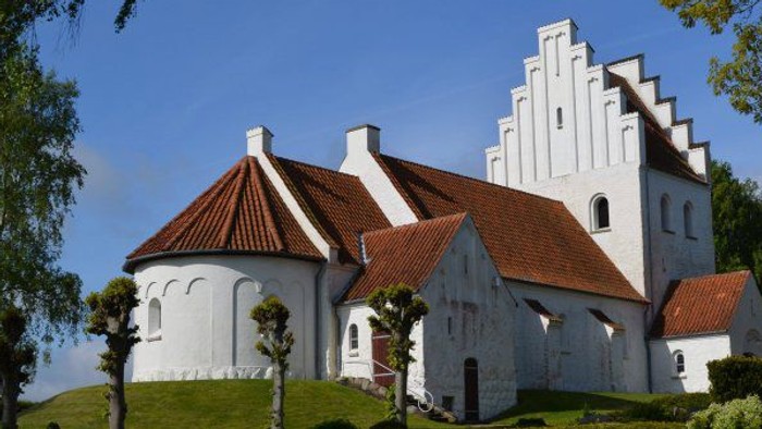 Et hvidt slot med røde tag og en flagstang med dansketegn på en grøn bakke