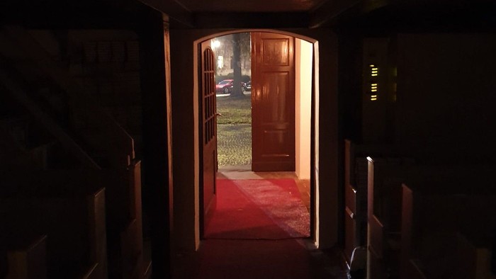 Dunkler Flur mit rotem Teppich, der zu offenen Holztüren führt.