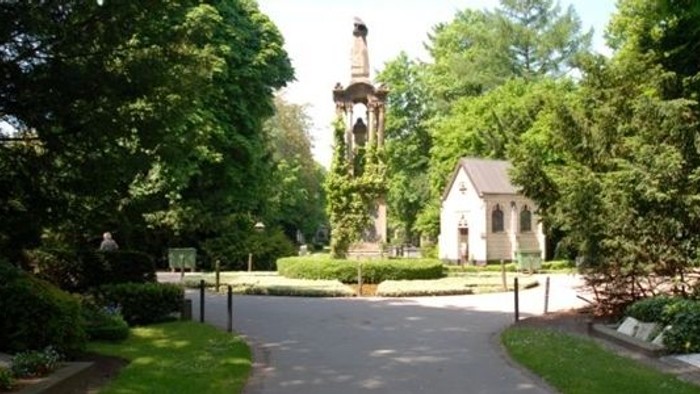 Ein gepflegter Park mit einem kleinen weißen Gebäude und einem hohen Turm im Hintergrund.