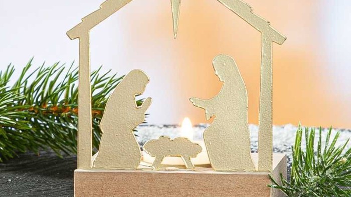 Et dekorativt krybbespil med silhuetfigurer under en krybbe med en stjerne på toppen, omgivet af fyrregrene og kunstig sne.