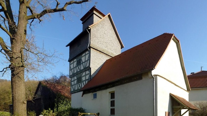 Weiße Kirche mit braunem Dach in der Nähe eines kahlen Baumes.