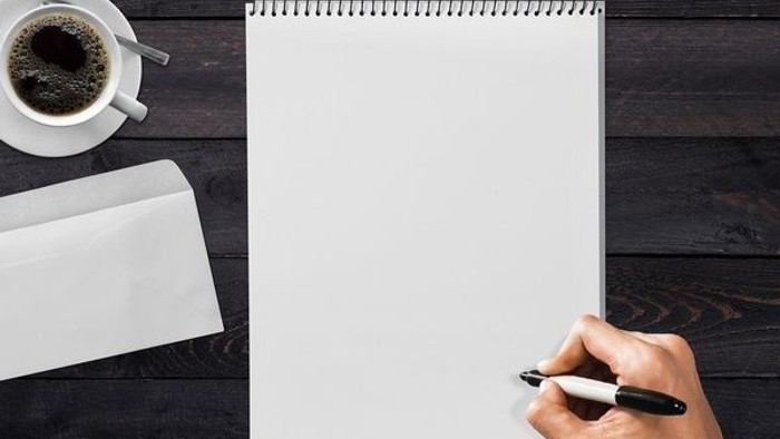 En hånd holder en marker over et blankt papir på en skrivebord med en kaffe og et brev.