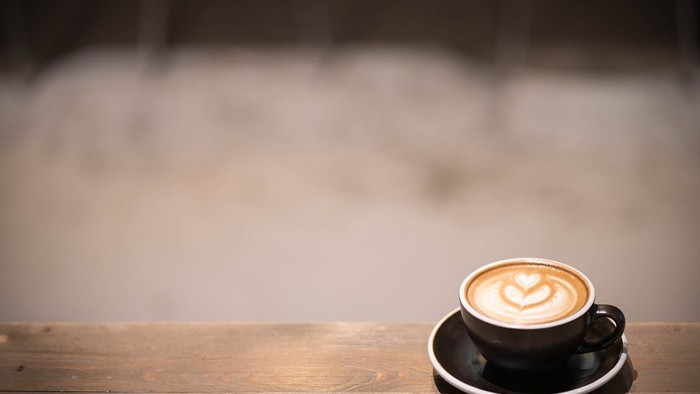 Ein Kaffeebecher mit Milchschaumherz auf einem Holztisch