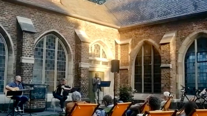 Ein Orchester spielt vor einem alten Backsteingebäude mit Bogenfenstern.