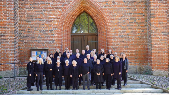 Ein großer Chor posiert vor einem Backsteingebäude mit einem großen Torbogen.